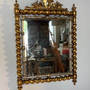 Specchiera antica dallo stile barocco, caratterizzata da una sontuosa cornice in legno intagliato con finitura dorata e dettagli argentati.