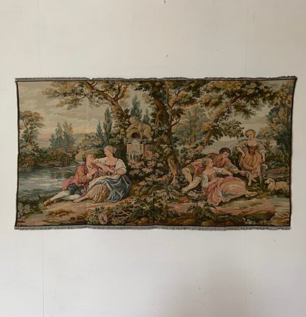Magnifico arazzo in stile rococò raffigura una scena bucolica incantevole, intrisa di eleganza e serenità. Un gruppo di dame e cavalieri si rilassa in un paesaggio lussureggiante